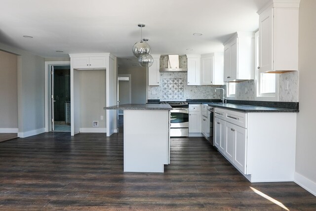 kitchen with stainless steel appliances, dark countertops, wall chimney exhaust hood, and white cabinets