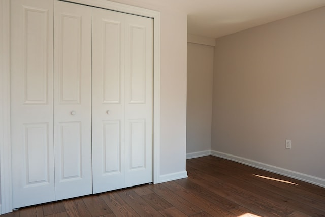 unfurnished bedroom with a closet, baseboards, and dark wood-style flooring