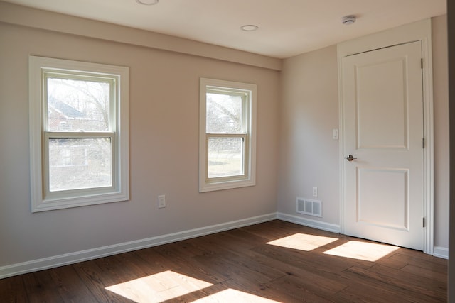 spare room with dark wood-style floors, visible vents, and baseboards