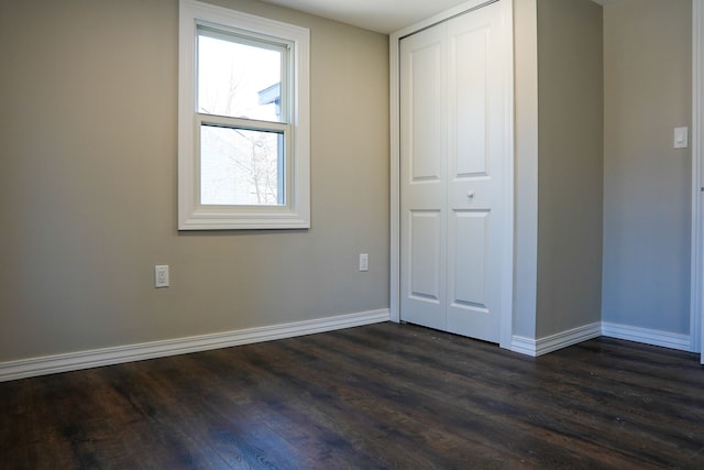 unfurnished bedroom featuring a closet, baseboards, and dark wood-style flooring