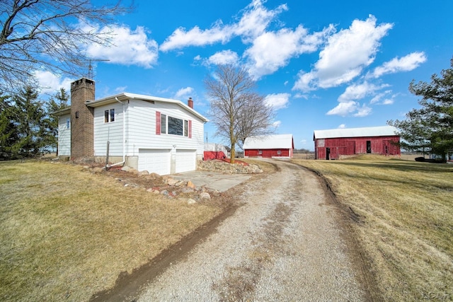 view of home's exterior with an attached garage, a yard, dirt driveway, and a chimney