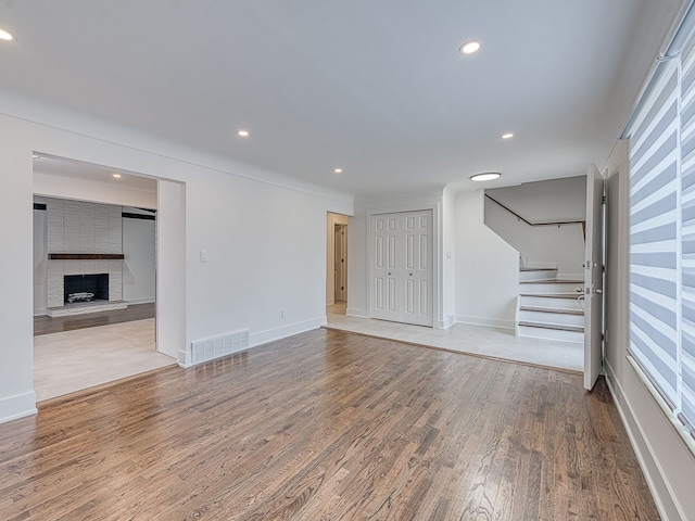 unfurnished living room featuring visible vents, stairs, recessed lighting, a fireplace, and wood finished floors