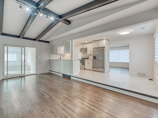 unfurnished living room with lofted ceiling with beams, light wood-style floors, visible vents, and baseboards