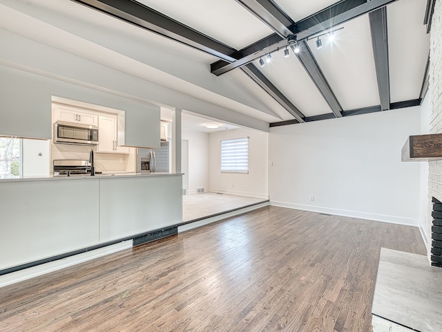 unfurnished living room with vaulted ceiling with beams, a fireplace, light wood-type flooring, and baseboards