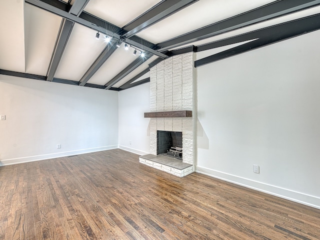 unfurnished living room with dark wood finished floors, rail lighting, a fireplace, baseboards, and vaulted ceiling with beams