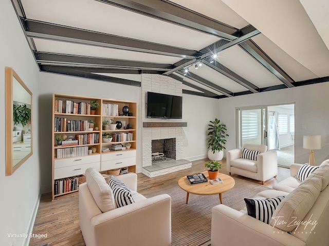 living area with baseboards, a brick fireplace, wood finished floors, and vaulted ceiling with beams