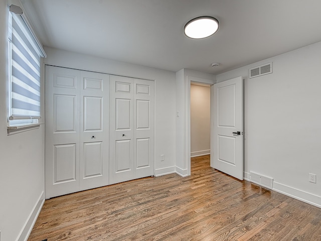 unfurnished bedroom featuring a closet, visible vents, baseboards, and wood finished floors