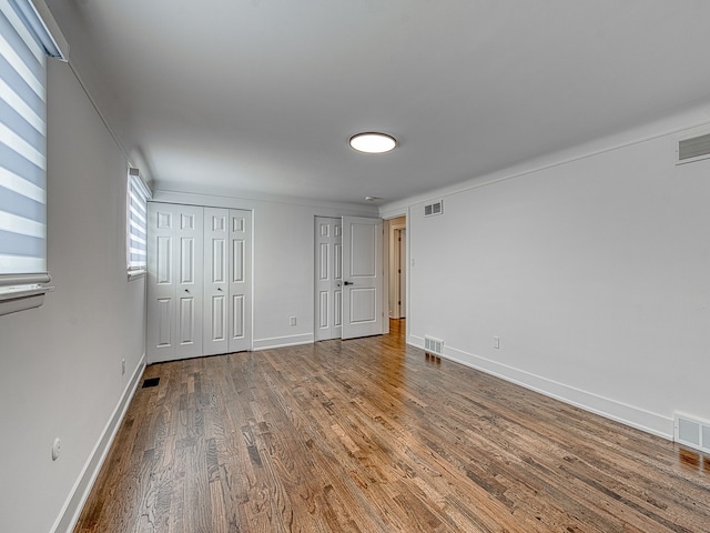 unfurnished bedroom with visible vents, two closets, baseboards, and wood finished floors