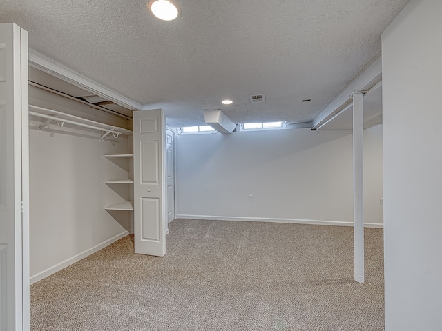 finished below grade area with visible vents, a textured ceiling, and carpet floors