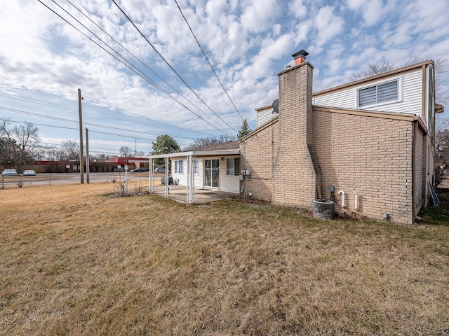 back of property featuring cooling unit, a chimney, a lawn, a patio area, and brick siding