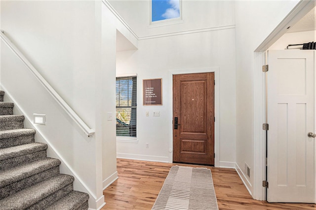 foyer featuring light wood-type flooring, baseboards, visible vents, and stairway