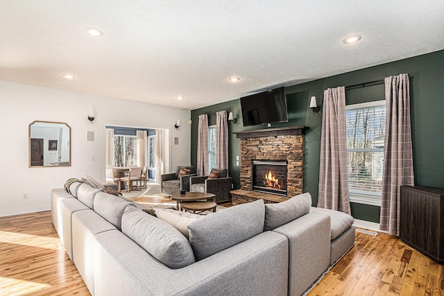 living room with light wood finished floors, visible vents, radiator, baseboards, and a stone fireplace