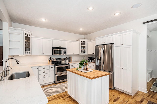 kitchen featuring butcher block countertops, light wood-style floors, white cabinets, stainless steel appliances, and a sink