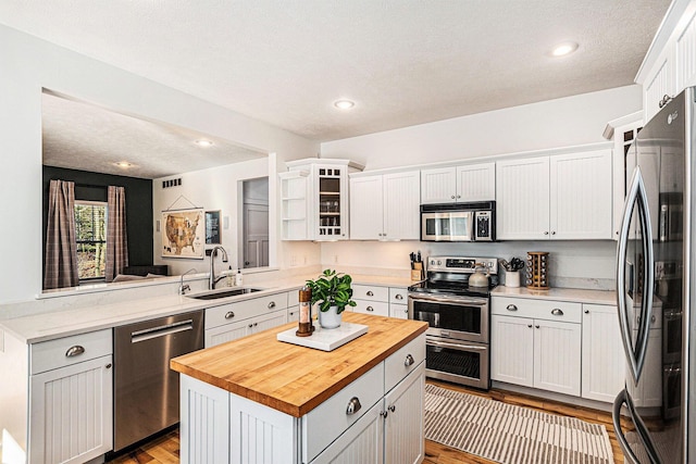 kitchen with butcher block countertops, appliances with stainless steel finishes, a peninsula, white cabinetry, and a sink