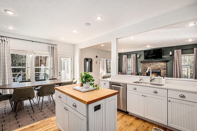 kitchen featuring butcher block countertops, a sink, a stone fireplace, light wood finished floors, and dishwasher