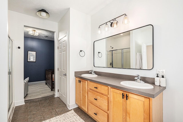 full bath with double vanity, a shower stall, baseboards, and a sink