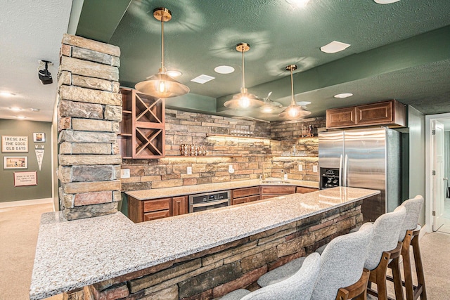 kitchen with carpet, light stone countertops, a peninsula, stainless steel appliances, and a textured ceiling