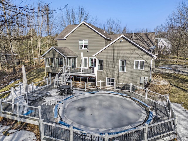 rear view of house with a deck, a trampoline, a shingled roof, outdoor dining area, and stairs