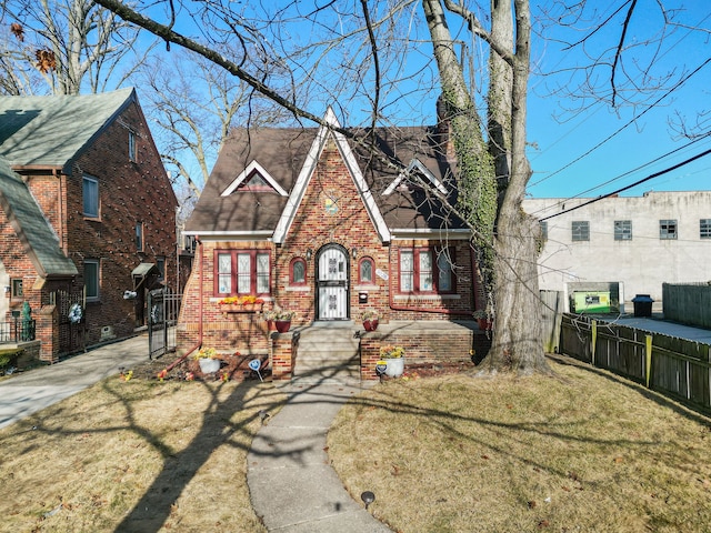 tudor home featuring brick siding, a front yard, and fence