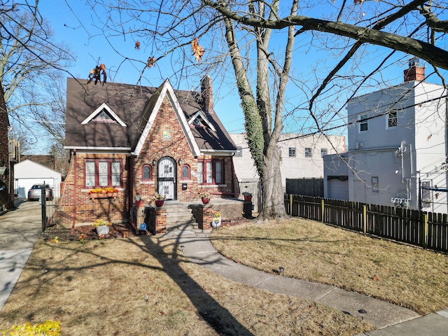 tudor home with an outbuilding, a front lawn, fence, brick siding, and a chimney