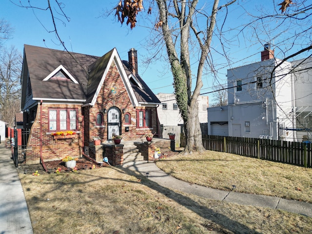 tudor house featuring brick siding, a chimney, a front lawn, and fence