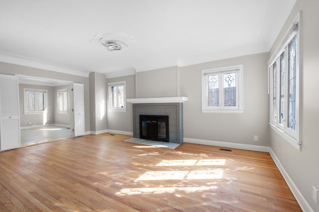 unfurnished living room featuring baseboards, light wood-type flooring, plenty of natural light, and a brick fireplace