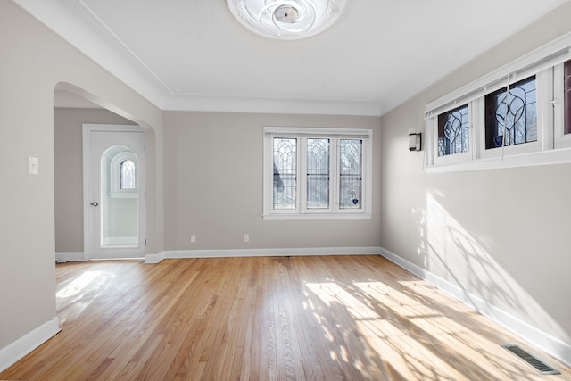 unfurnished room featuring arched walkways, visible vents, light wood finished floors, and baseboards