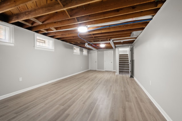 basement featuring stairway, light wood-type flooring, and baseboards