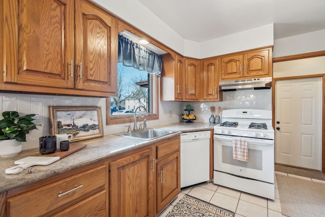 kitchen with white appliances, light tile patterned floors, brown cabinetry, a sink, and under cabinet range hood