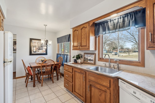 kitchen with pendant lighting, light countertops, brown cabinetry, white appliances, and a sink