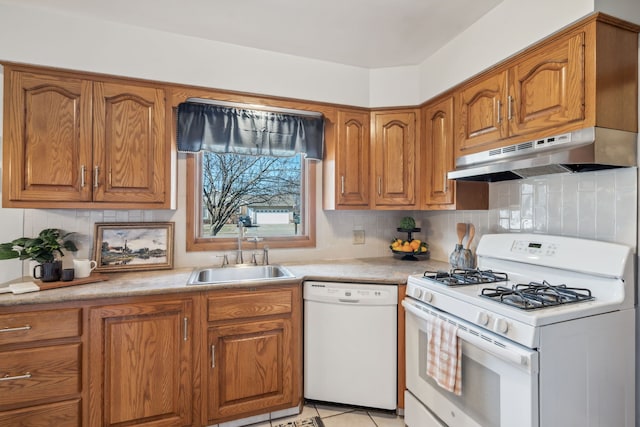 kitchen with under cabinet range hood, white appliances, brown cabinetry, and a sink