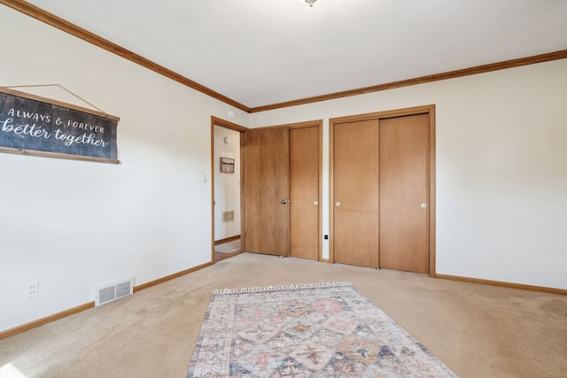 unfurnished bedroom with crown molding, visible vents, two closets, and light carpet