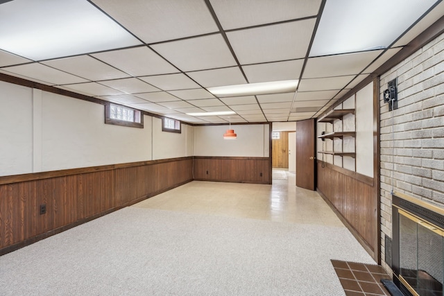 basement featuring a wainscoted wall, wood walls, a drop ceiling, carpet floors, and a fireplace