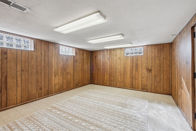 basement with visible vents, a textured ceiling, light floors, and wood walls