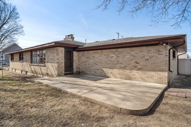 rear view of property with fence, brick siding, a chimney, and a patio area