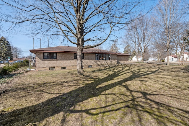 back of house with brick siding, a lawn, and fence