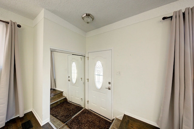 foyer with visible vents, baseboards, a textured ceiling, and dark wood finished floors