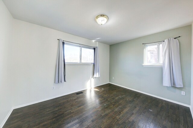 unfurnished room with visible vents, dark wood-type flooring, and baseboards