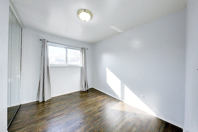 empty room with dark wood finished floors, visible vents, and baseboards