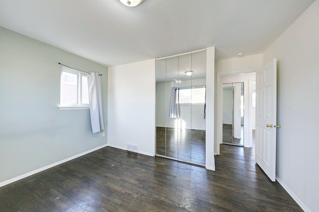 unfurnished bedroom with visible vents, multiple windows, baseboards, and dark wood-style floors