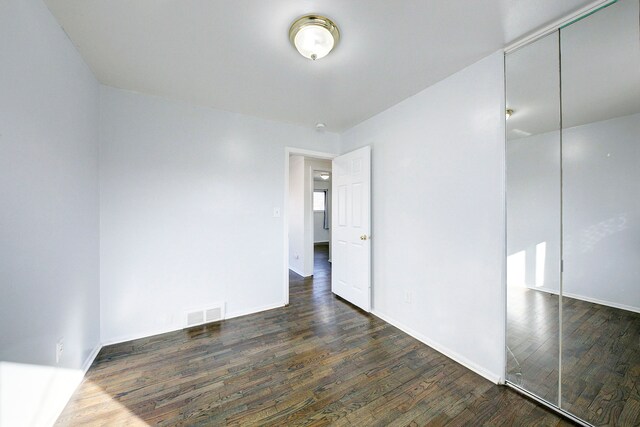 unfurnished bedroom featuring a closet, baseboards, dark wood-type flooring, and visible vents