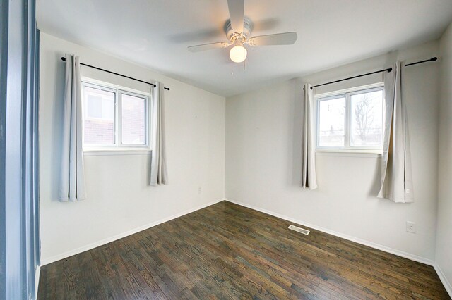 empty room featuring ceiling fan, baseboards, plenty of natural light, and dark wood-style floors