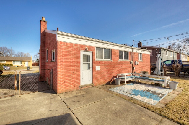 rear view of house featuring fence, brick siding, a chimney, and a patio area