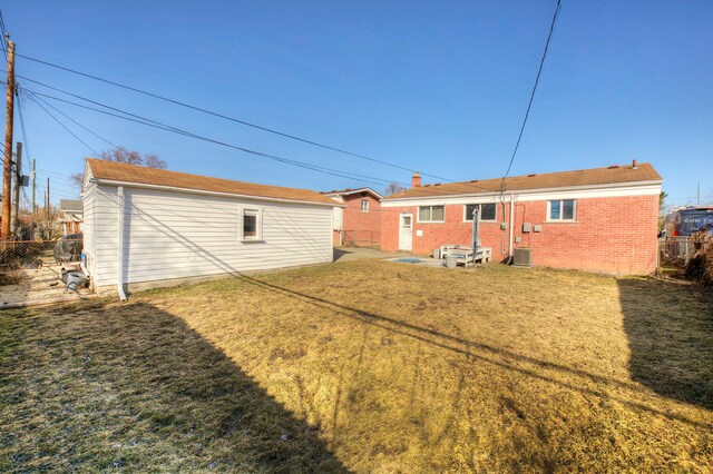 rear view of house with brick siding, fence, central AC unit, a lawn, and an outbuilding