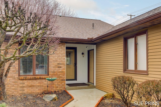 entrance to property featuring brick siding and roof with shingles