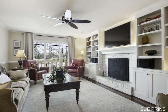 living area featuring ornamental molding, a ceiling fan, built in features, wood finished floors, and a fireplace