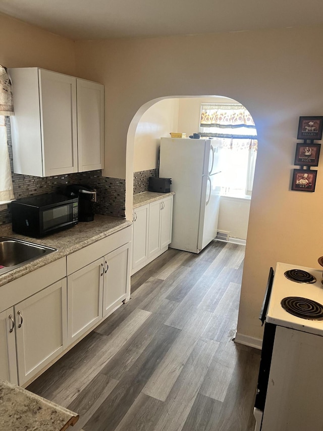 kitchen featuring white cabinetry, white appliances, wood finished floors, and tasteful backsplash