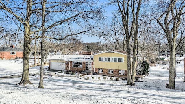 snow covered back of property with an attached garage, brick siding, and driveway