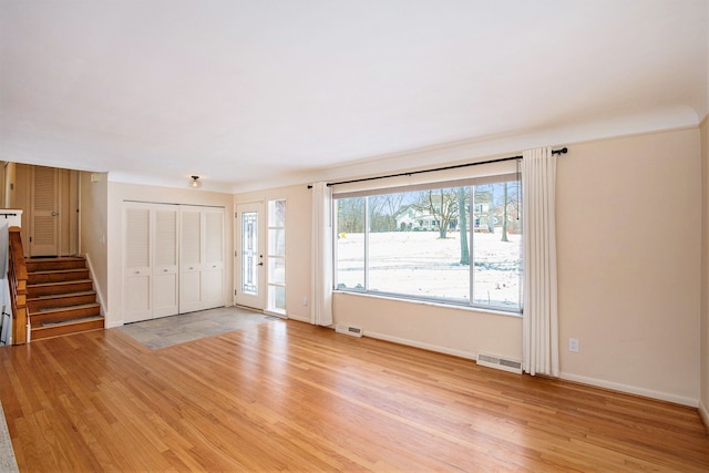 unfurnished living room with visible vents, baseboards, light wood-style floors, and stairway