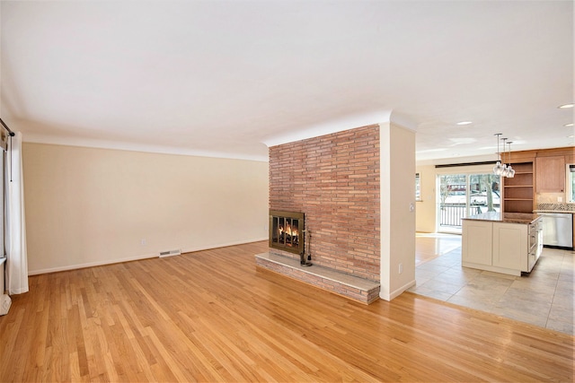 unfurnished living room featuring visible vents, a fireplace, light wood-style floors, and baseboards